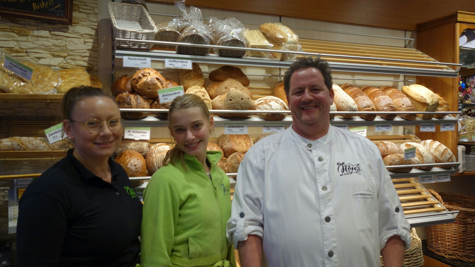 Zwei Verkäuferinnen und Inhaber Jörg Nöres stehen vor der gefüllten Brotauslage der Bäckerei Nöres.
