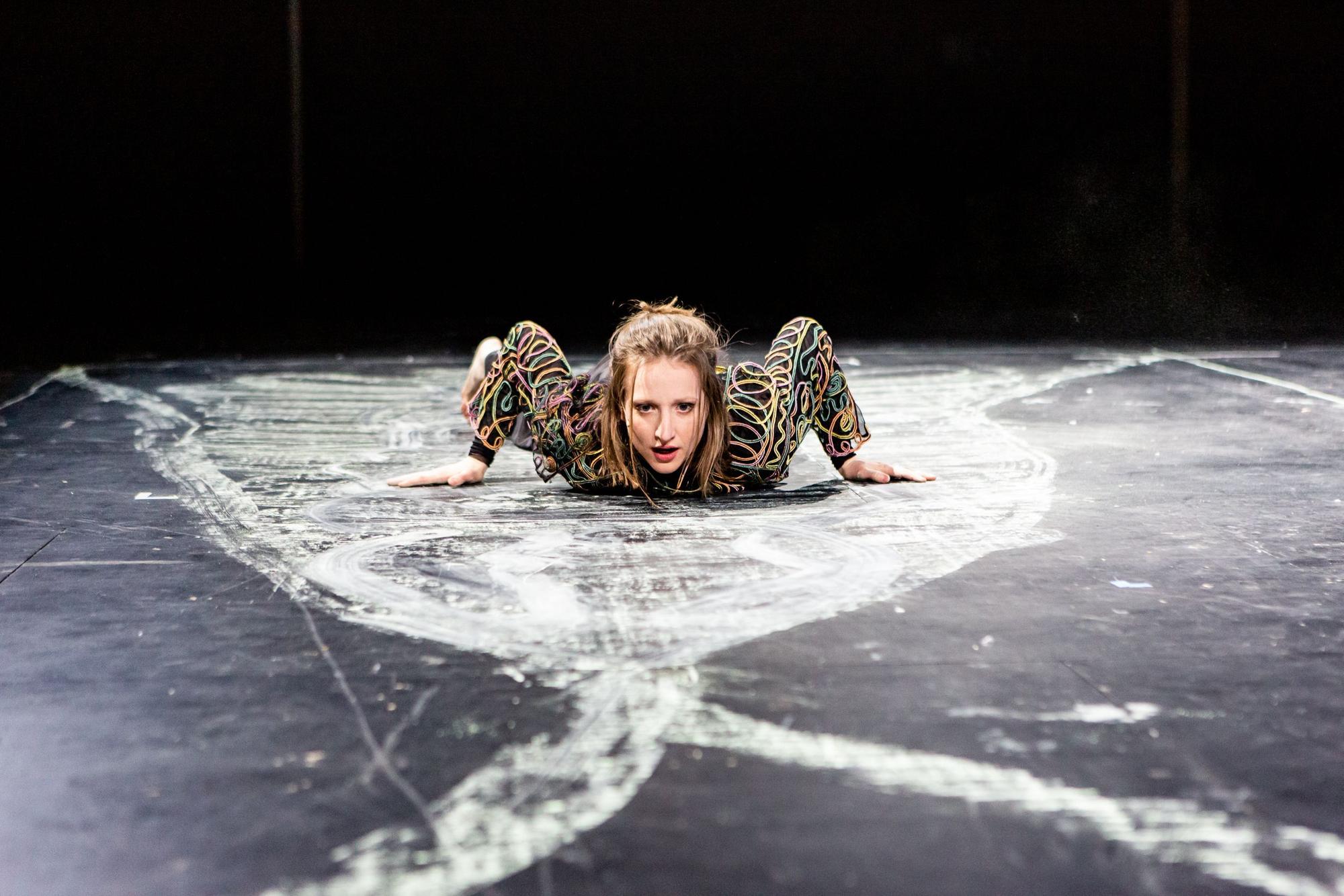 Die Schauspielerin Kristin Steffen liegt auf einem schwarzen Boden, der mit weißer Kreide bemalt ist.