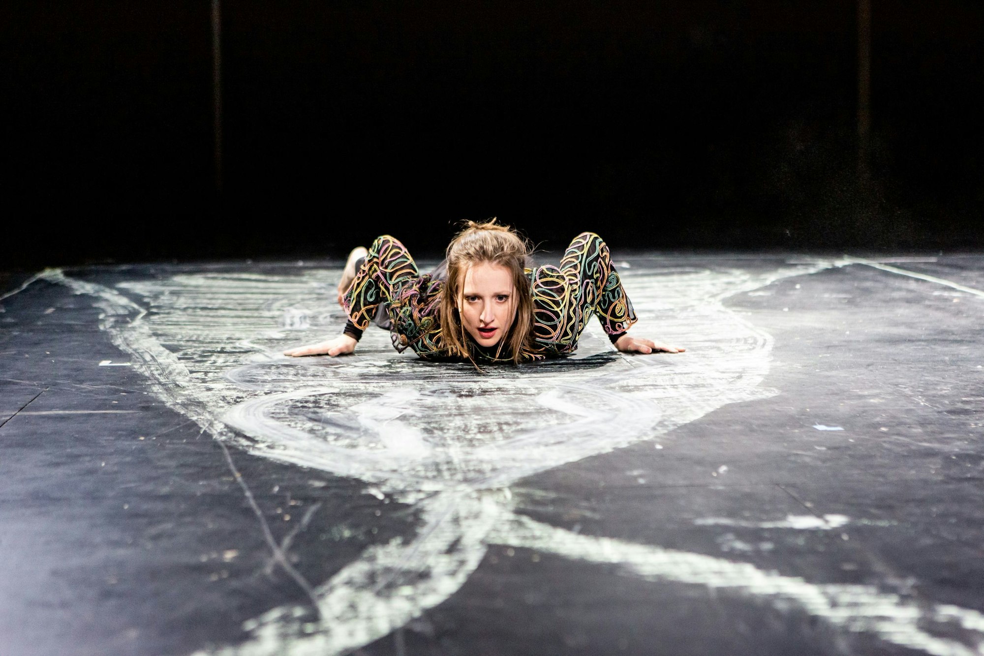Die Schauspielerin Kristin Steffen liegt auf einem schwarzen Boden, der mit weißer Kreide bemalt ist.