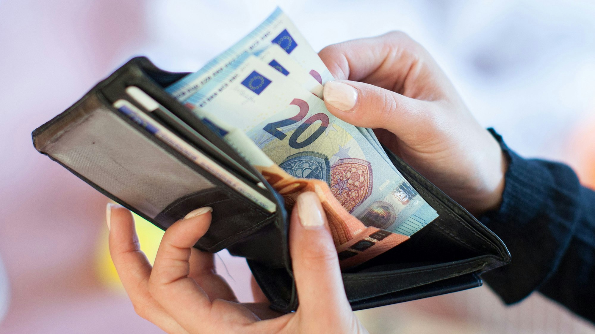 Eine Frau nimmt Banknoten aus einem Geldbeutel.