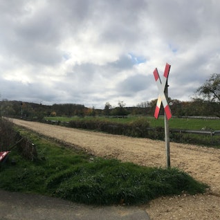 Auf der Bahnstrecke liegen keine Gleise. Neben der Strecke liegt ein Haus. Davor stehen Autos.