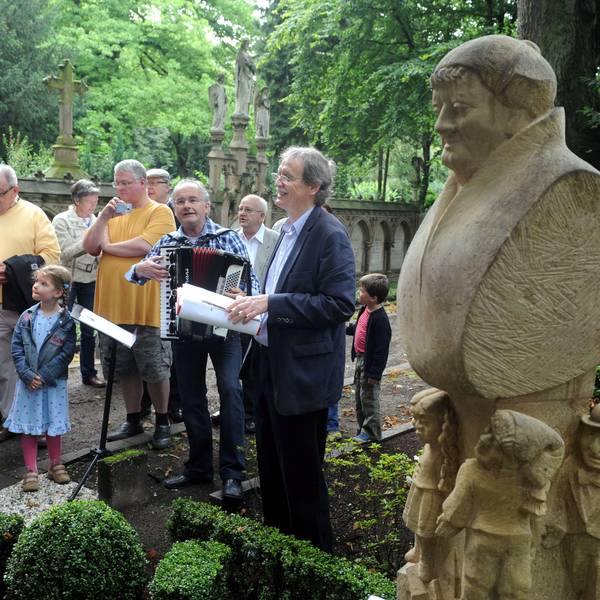 An der Gedenkstätte für Johann Christoph Winters, den Gründer des Hänneschen-Theaters, auf dem Melatenfriedhof haben sich mehrere Menschen versammelt. Zu sehen ist auch unser Autor Wolfgang Oelsner, der eine Rede hält.