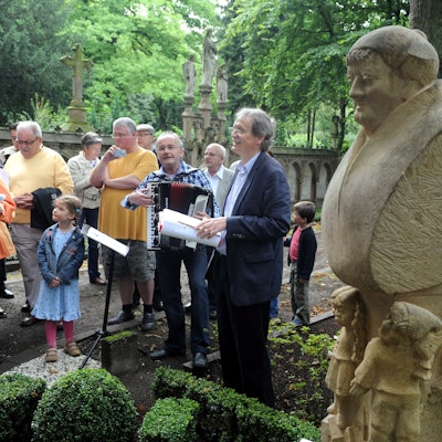 An der Gedenkstätte für Johann Christoph Winters, den Gründer des Hänneschen-Theaters, auf dem Melatenfriedhof haben sich mehrere Menschen versammelt. Zu sehen ist auch unser Autor Wolfgang Oelsner, der eine Rede hält.