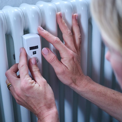 Eine Frau kontrolliert einen Heizkostenverteiler an der Heizung. (Symbolbild)