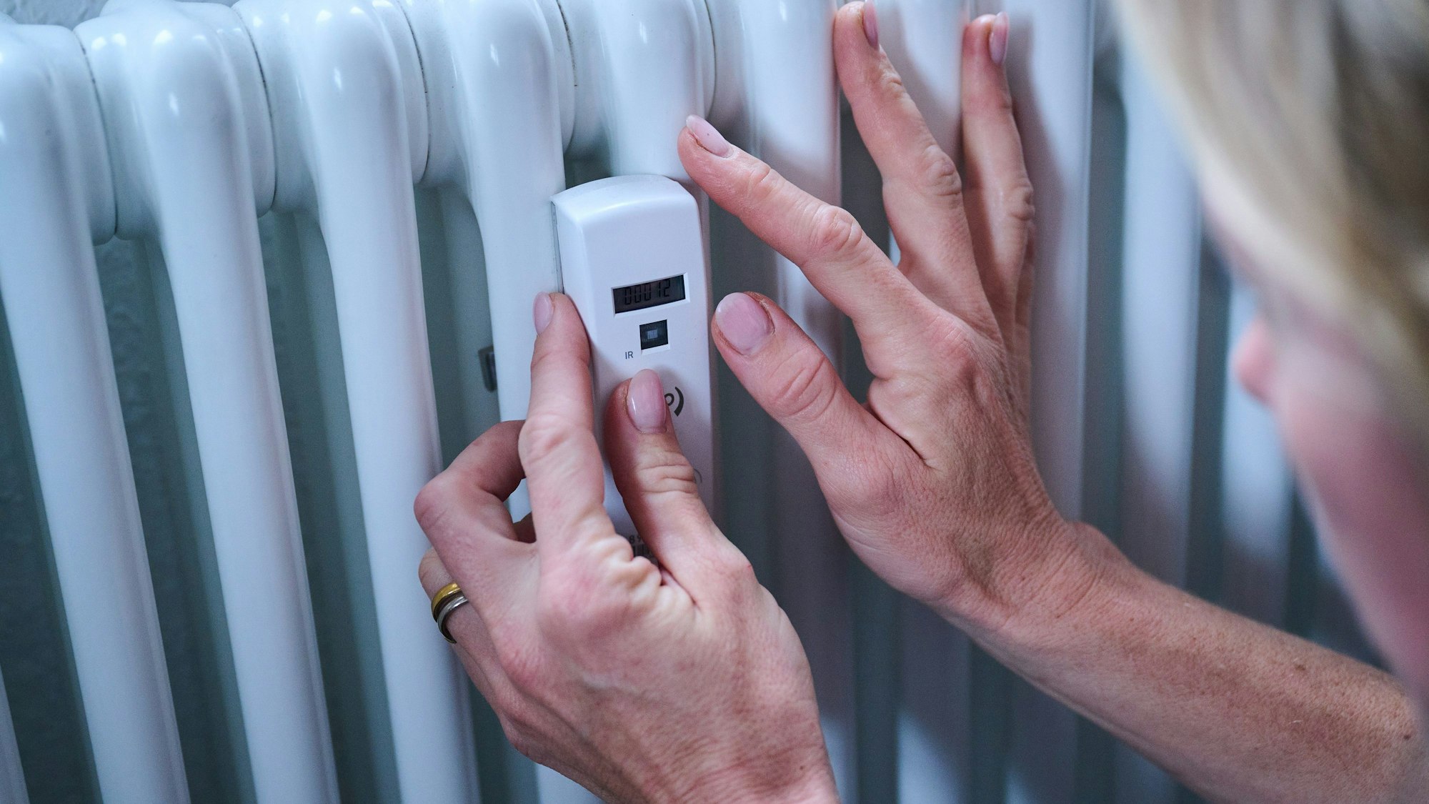 Eine Frau kontrolliert einen Heizkostenverteiler an der Heizung. (Symbolbild)