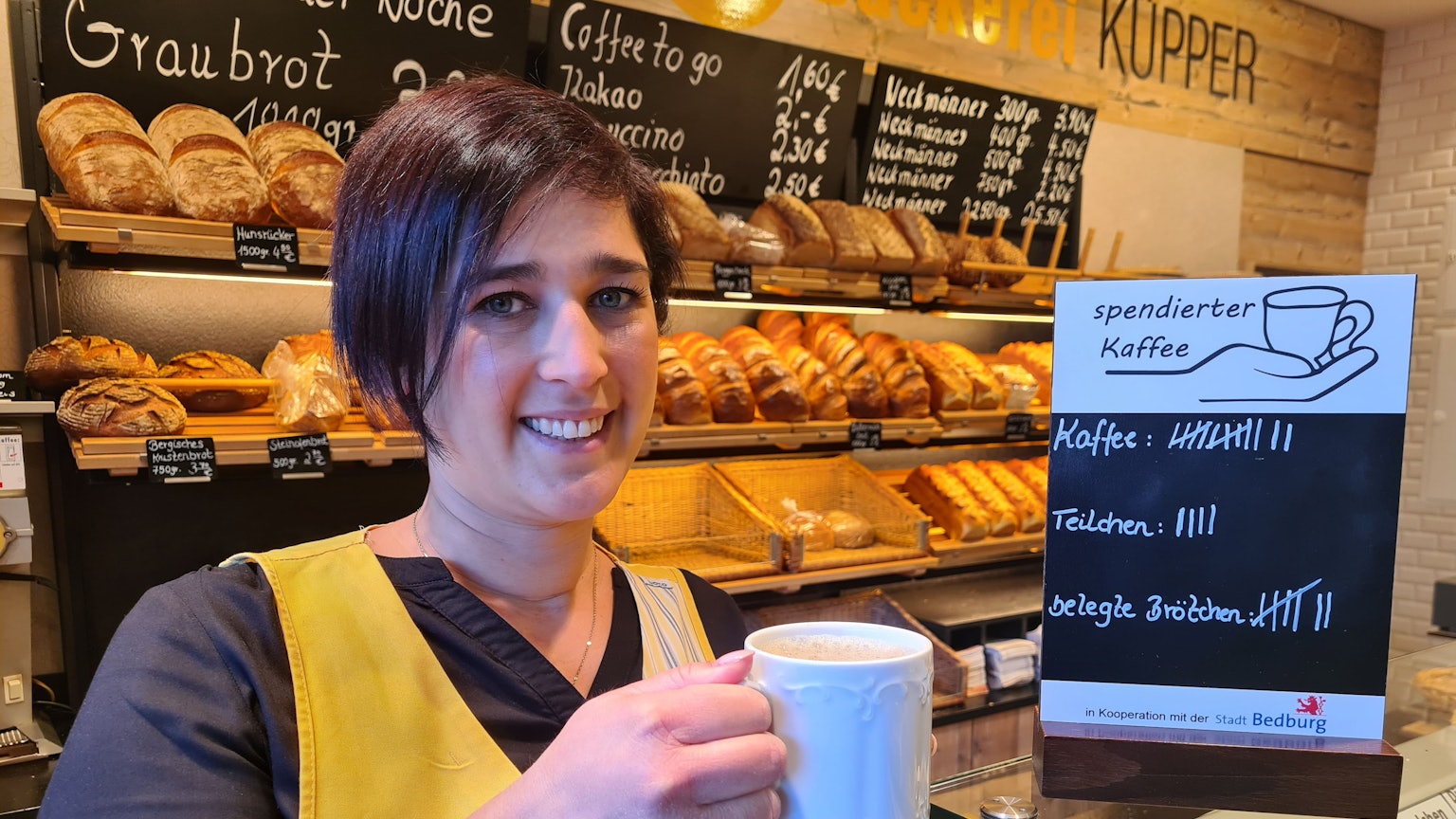 Jessica Küpper hält einen Kaffee in der Hand und steht vor dem Brotregal der Bäckerei Küpper in Bedburg.