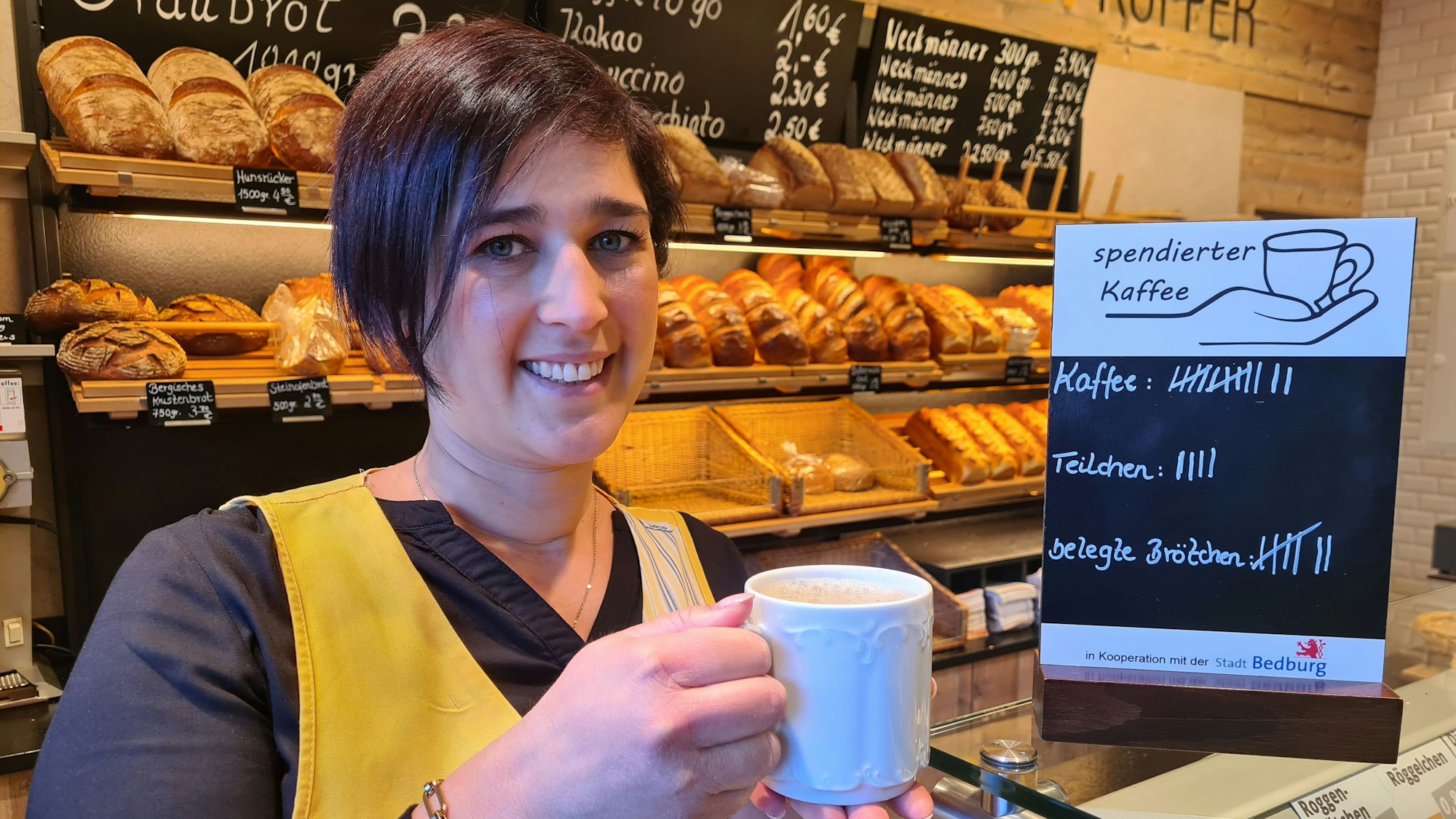 Jessica Küpper hält einen Kaffee in der Hand und steht vor dem Brotregal der Bäckerei Küpper in Bedburg.