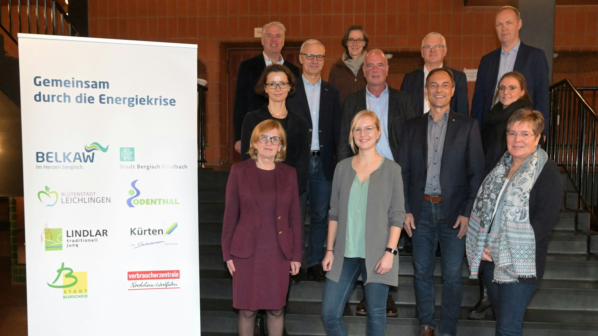 Die Beteiligten des Projekts „Gemeinsam durch die Energiekrise“ haben sich im Bergisch Löwen an einer Treppe zum Pressefoto aufgestellt.