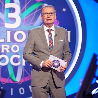 Moderator Günther Jauch steht in der Kulisse der RTL-Quizshow „Wer wird Millionär“ und hält eine Moderationskarte in der Hand.
