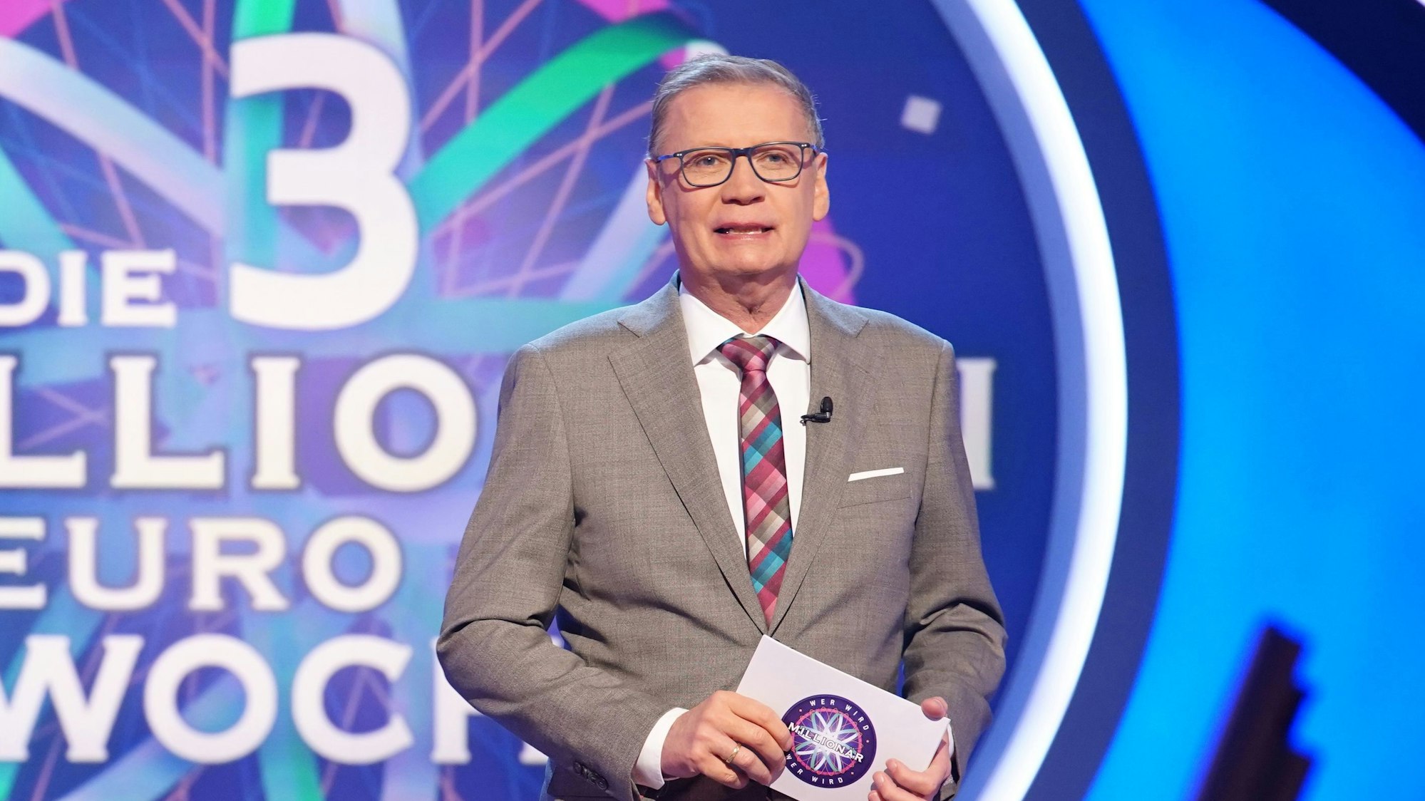 Moderator Günther Jauch steht in der Kulisse der RTL-Quizshow „Wer wird Millionär“ und hält eine Moderationskarte in der Hand.