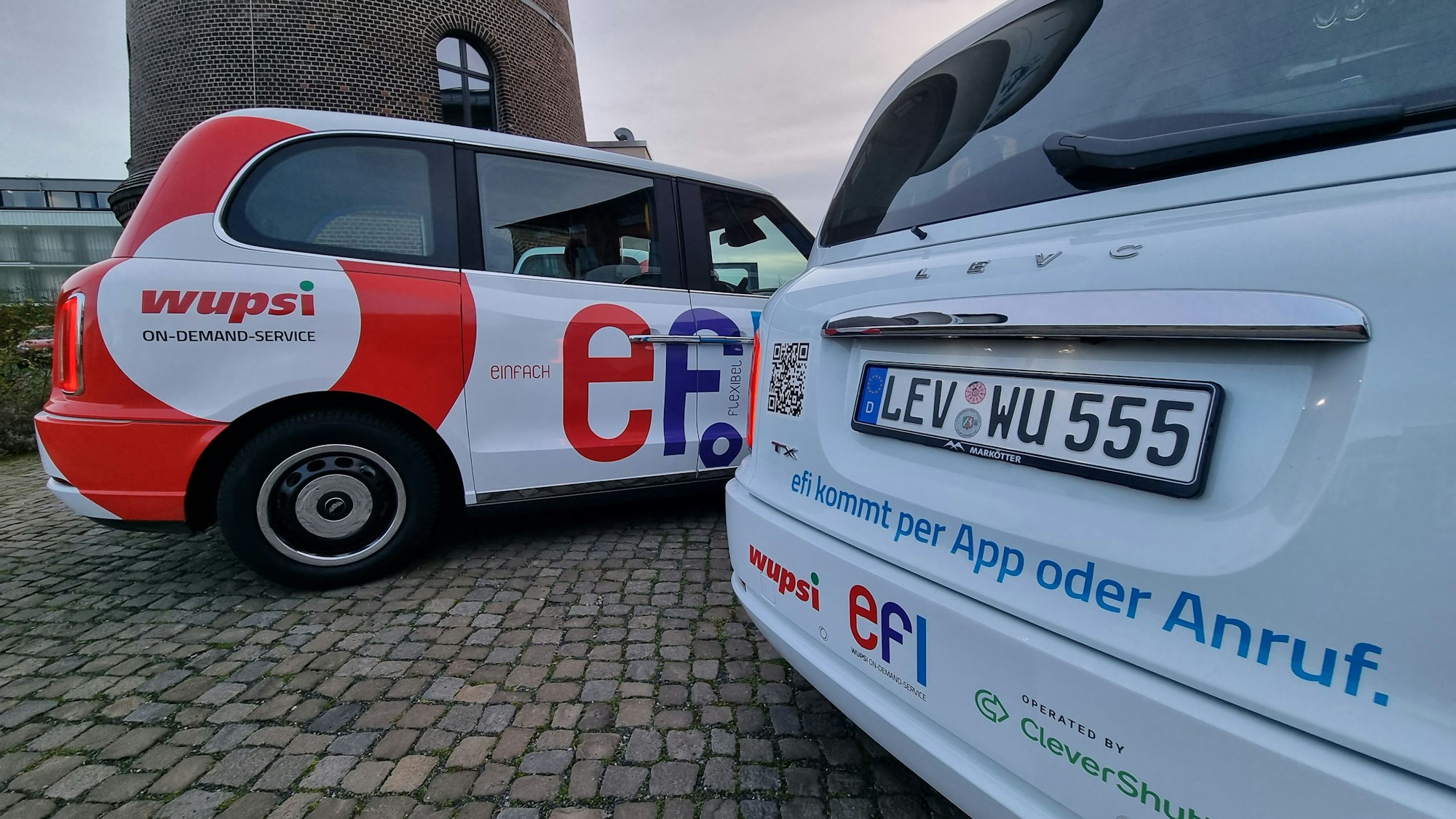 Zwei Kleinbusse des Efi-Systems stehen auf dem Platz vor dem Funkenturm in Opladen.