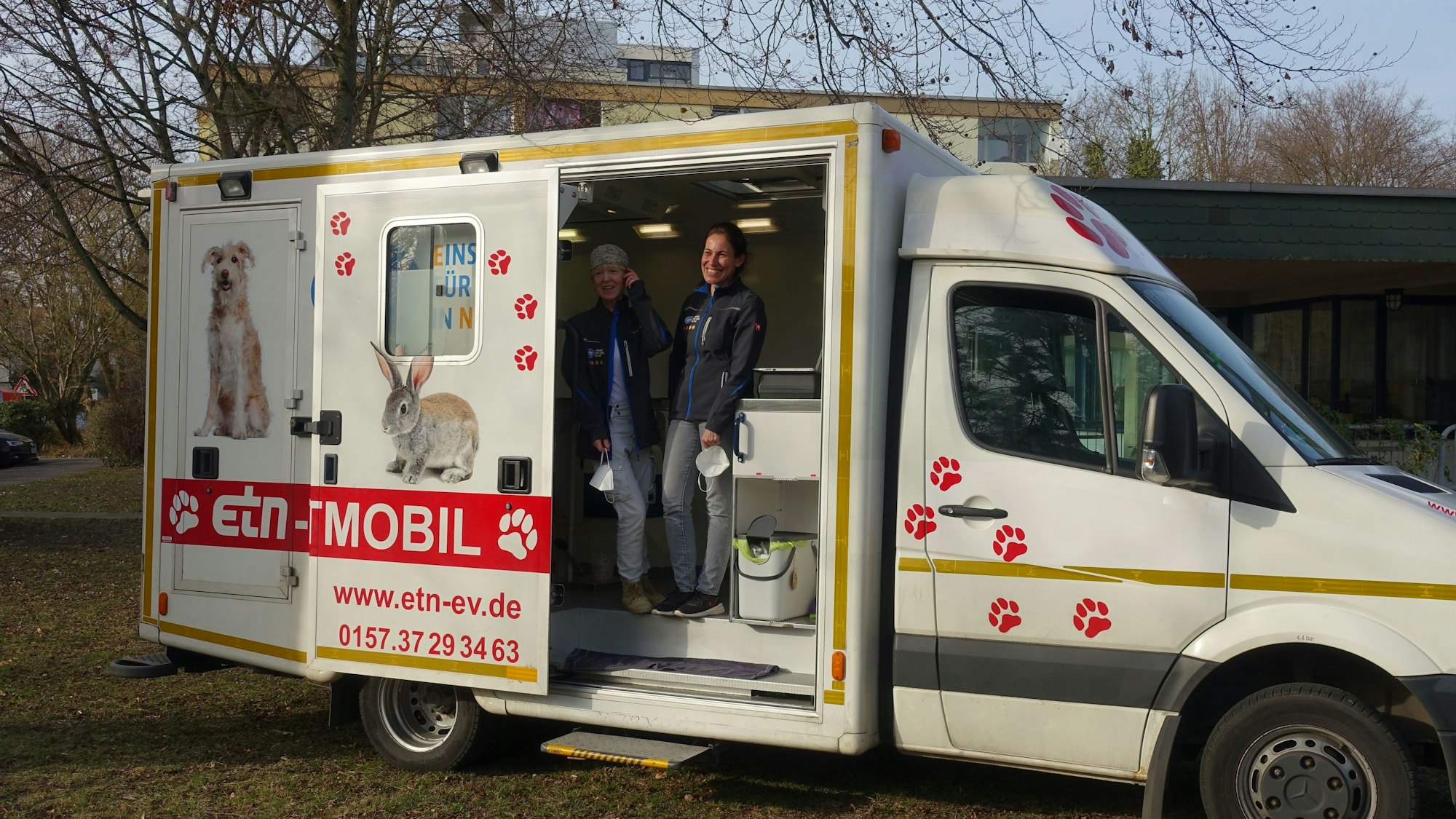 Ein Transporter ist bedruckt mit Hund und Kaninchen und vielen Pfoten. Im Inneren stehen zwei Frauen und lächeln.