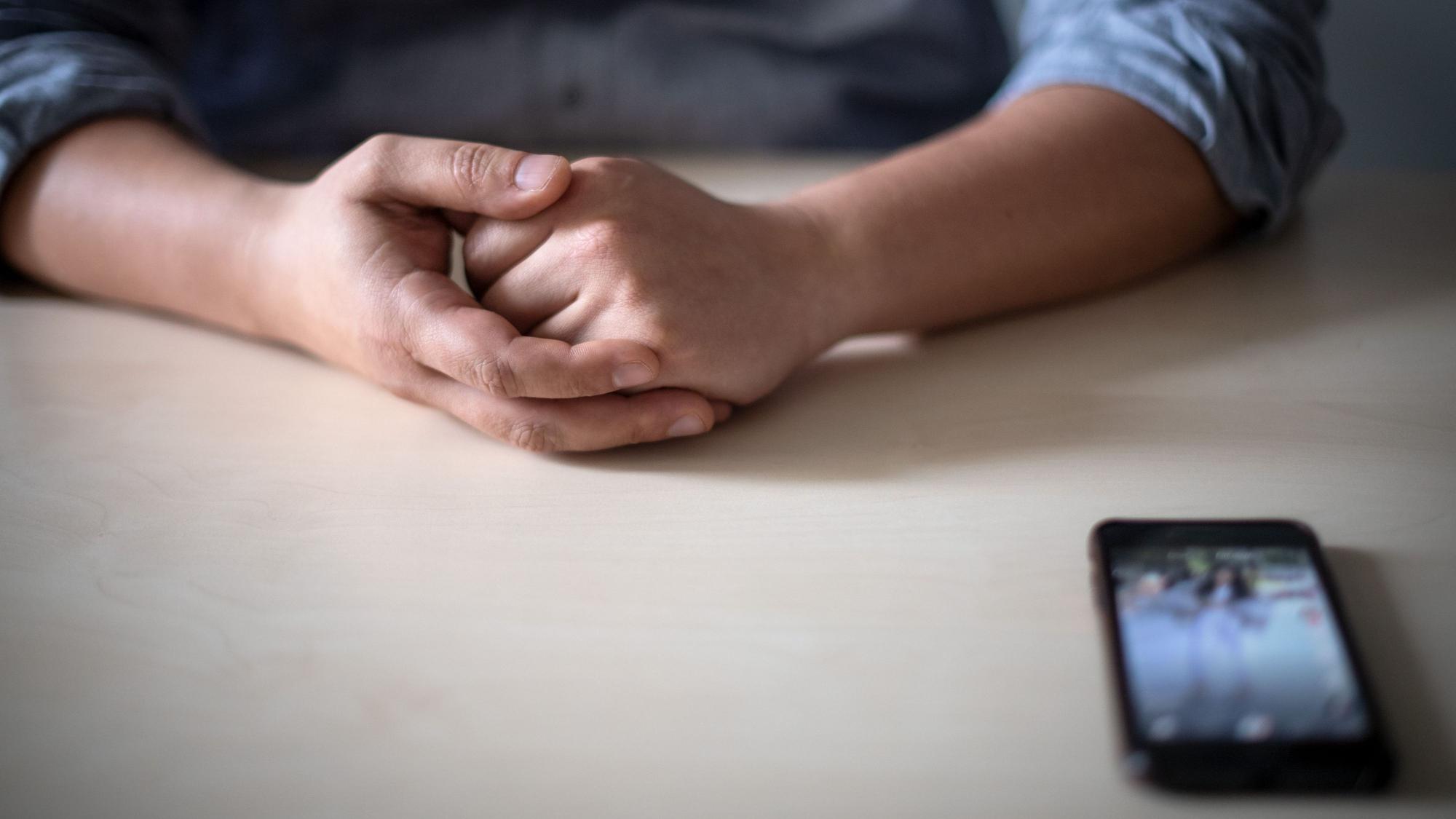 Ein Smartphone liegt vor einem jungen Mann auf dem Tisch.