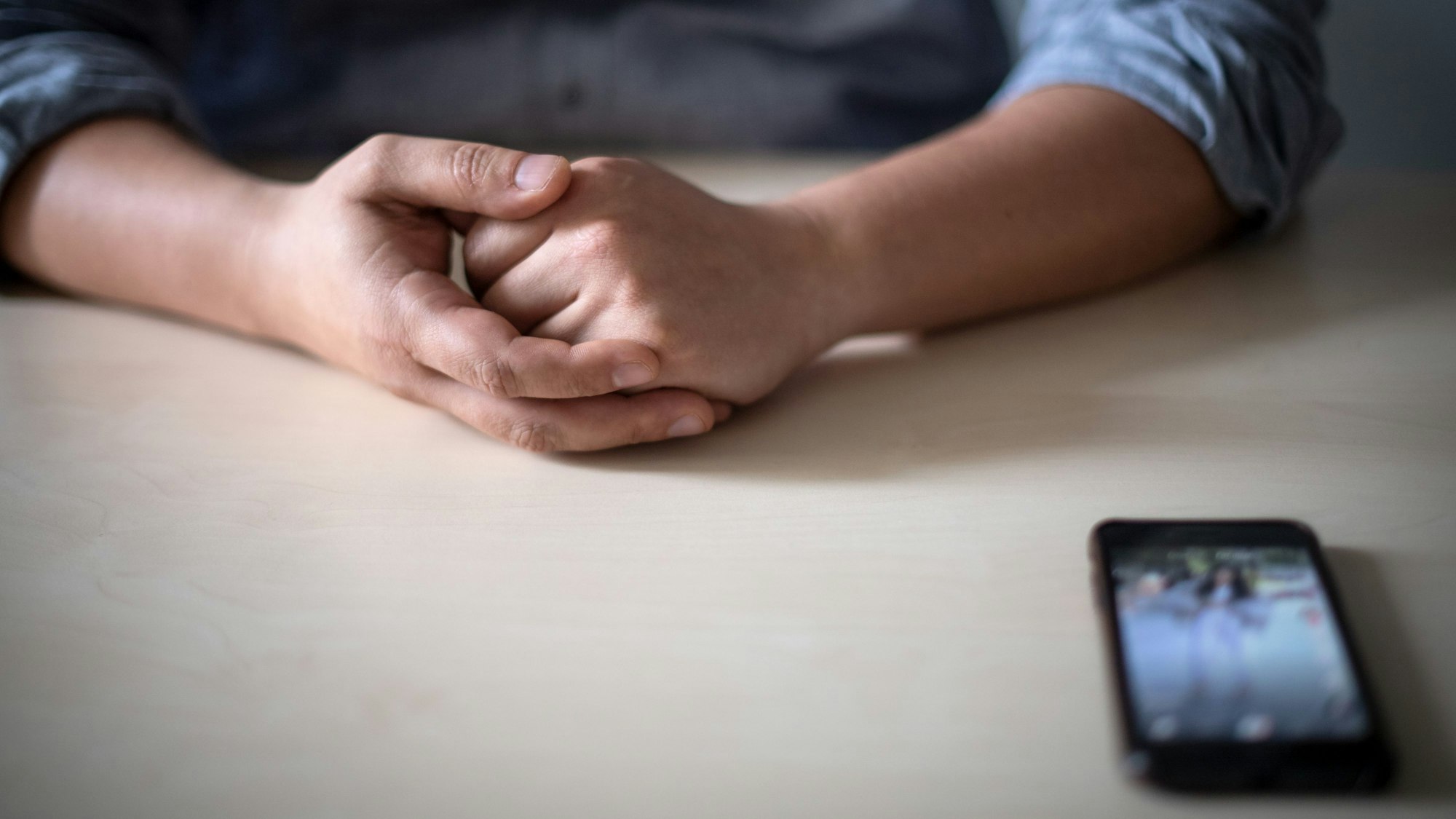 Ein Smartphone liegt vor einem jungen Mann auf dem Tisch.