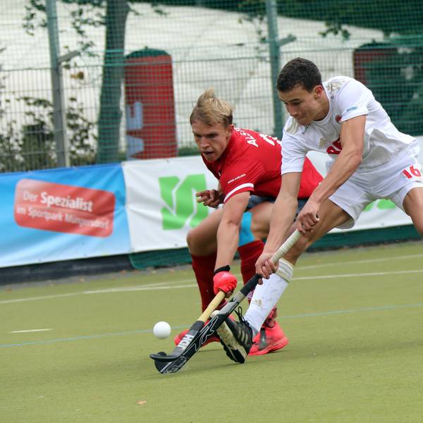 Zwei Hockeyspieler im Zweikampf, der rechte spitzelt dem linken den Ball weg.
