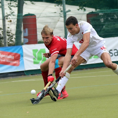 Zwei Hockeyspieler im Zweikampf, der rechte spitzelt dem linken den Ball weg.