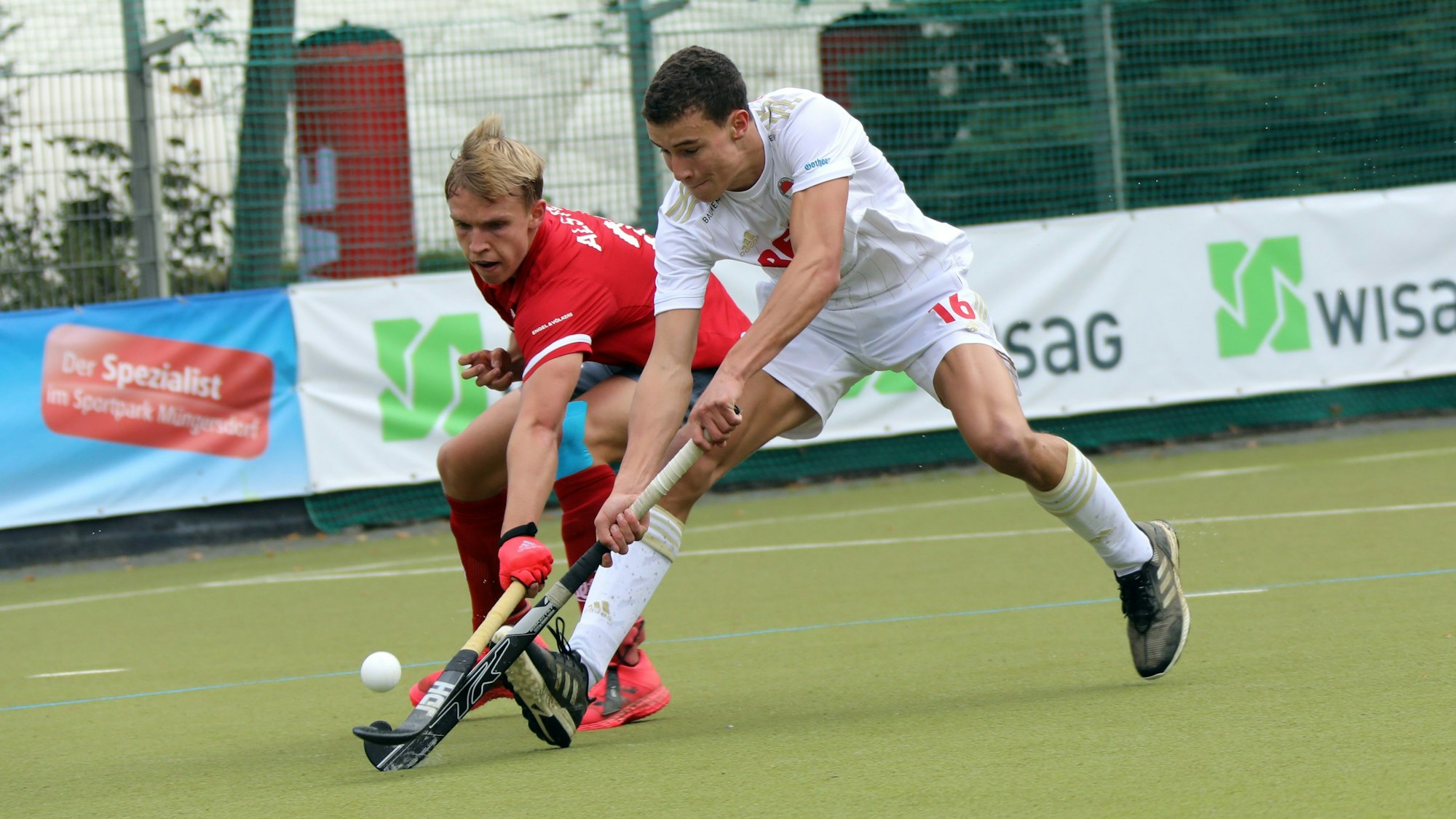 Zwei Hockeyspieler im Zweikampf, der rechte spitzelt dem linken den Ball weg.