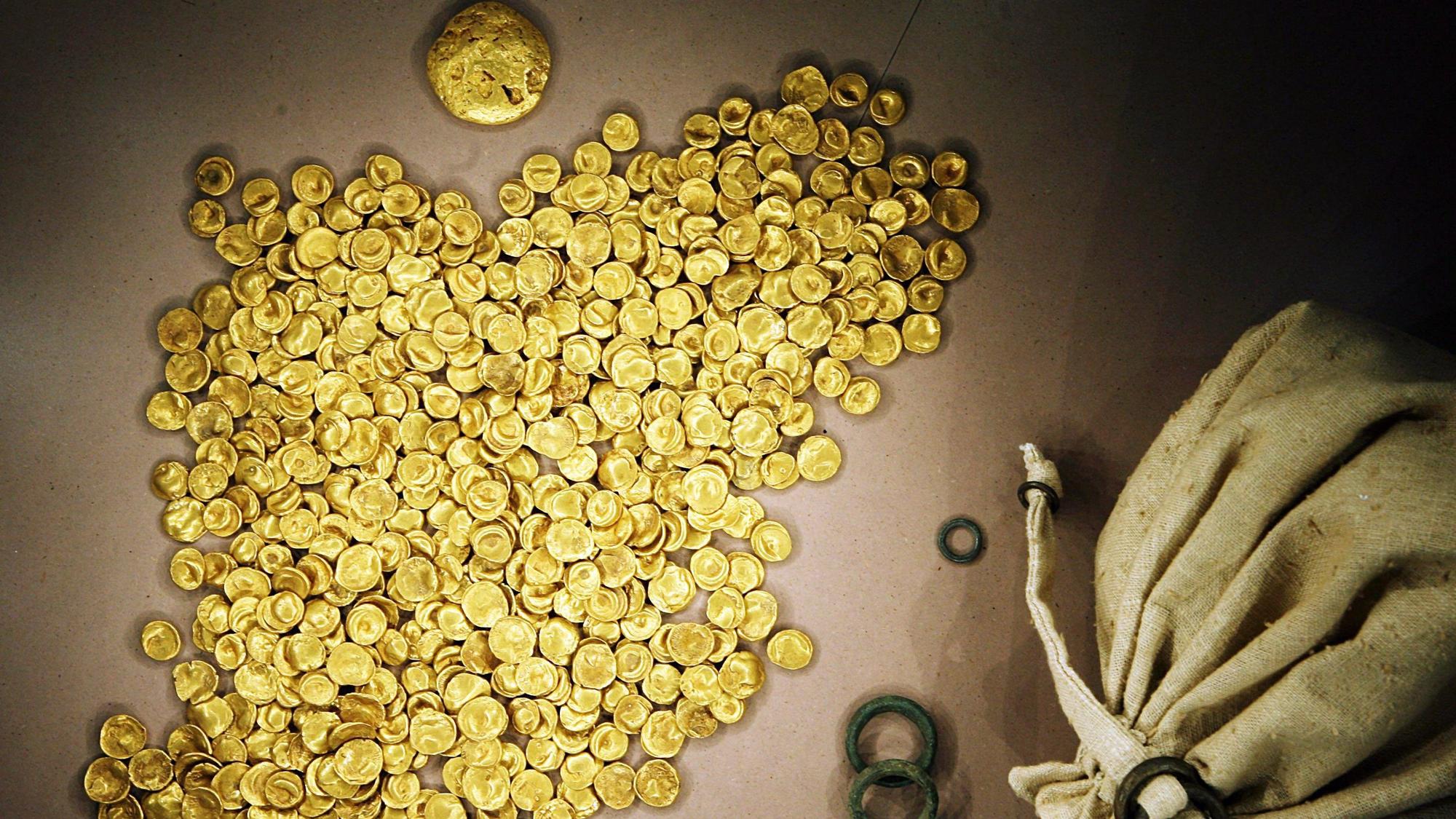 Ein Haufen Goldstücke liegt neben einem Beutel auf einer Oberfläche. (Symbolbild)