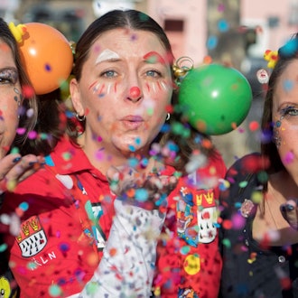 Drei weibliche Jecken haben sich bunt kostümiert und pusten Konfetti in die Luft.