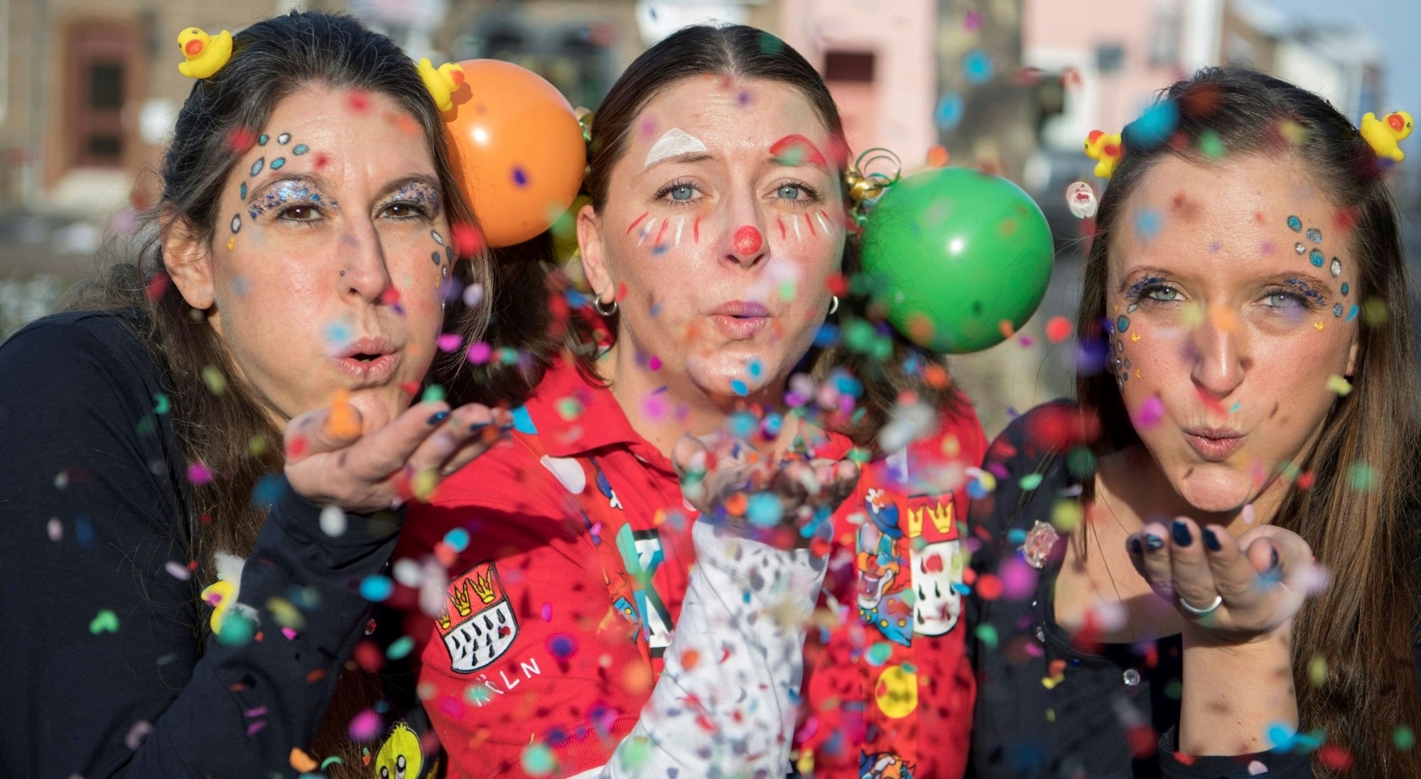 Drei weibliche Jecken haben sich bunt kostümiert und pusten Konfetti in die Luft.
