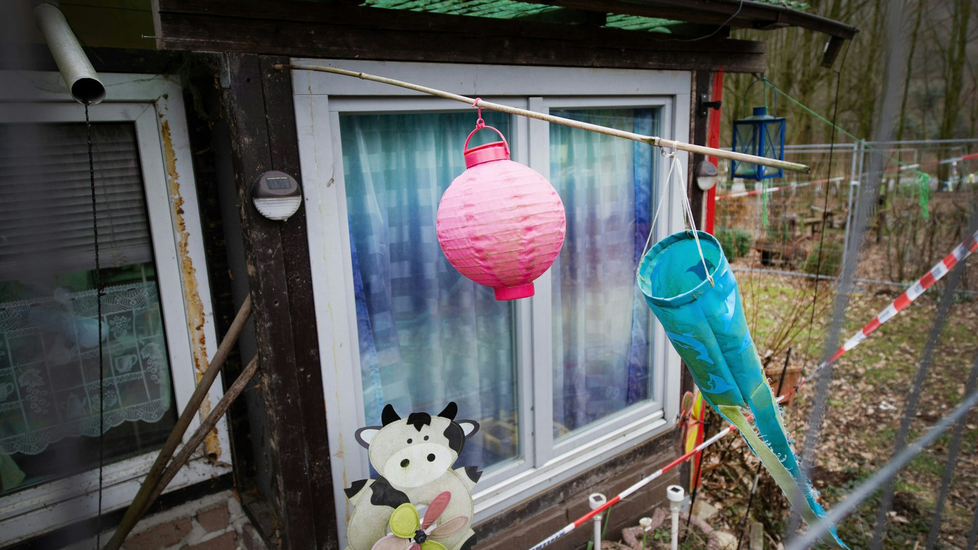 Hinter einem Zaun und Polizeiabsperrband ist ein Lampion und ein Windspiel auf dem Campingplatz Eichwald zu sehen. (Archivbild)