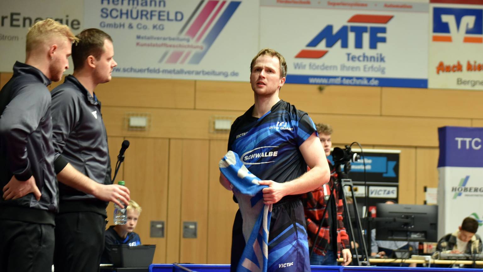 Ein Spieler der TTC Schwalbe steht neben den Trainern mit einem Handtuch in der Hand.
