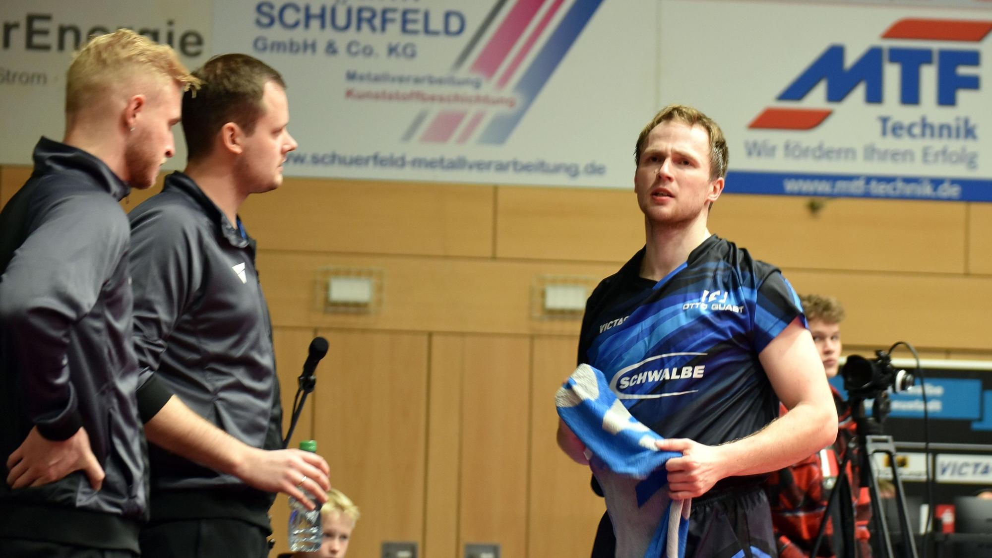 Ein Spieler der TTC Schwalbe steht neben den Trainern mit einem Handtuch in der Hand.