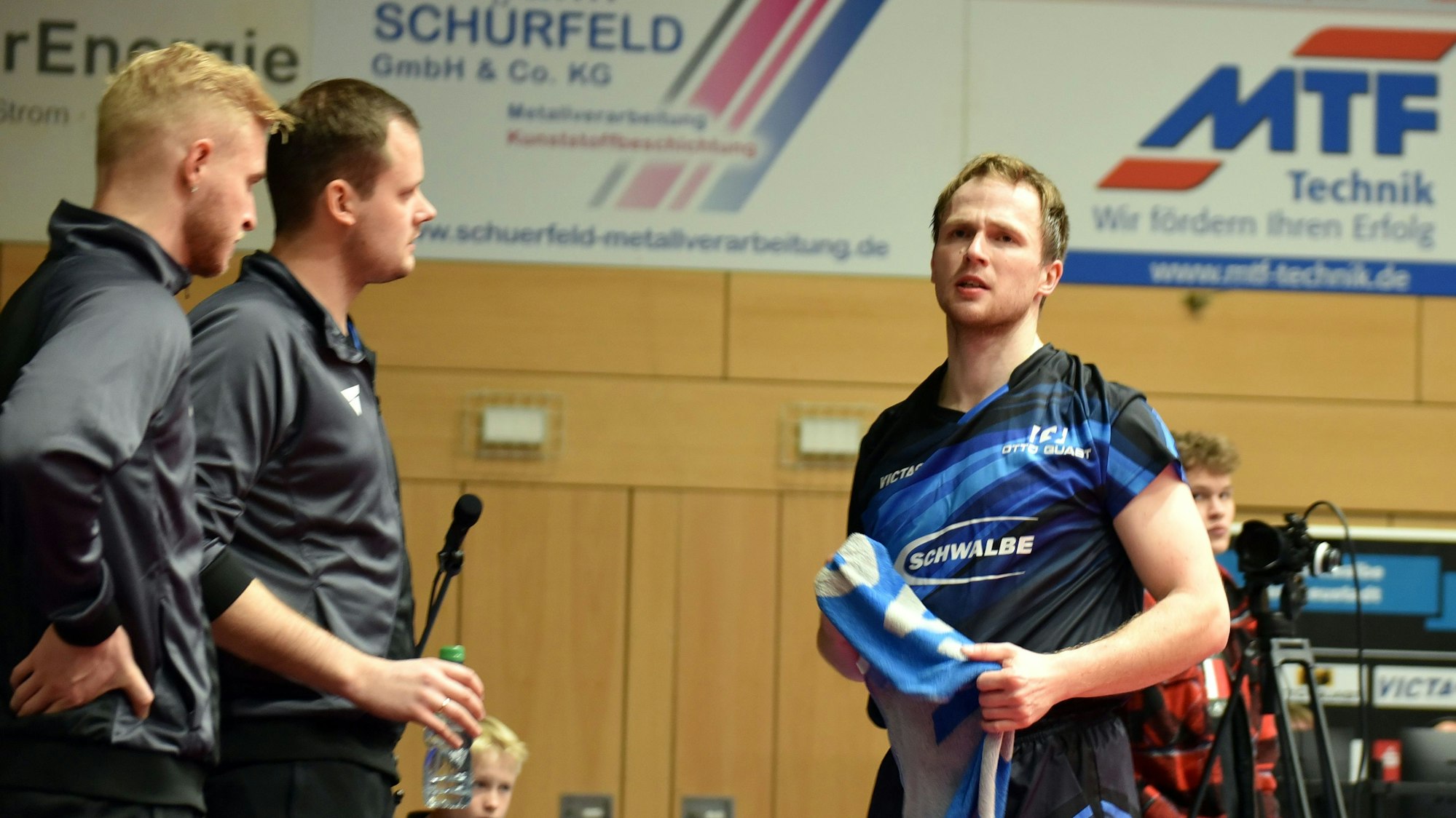 Ein Spieler der TTC Schwalbe steht neben den Trainern mit einem Handtuch in der Hand.