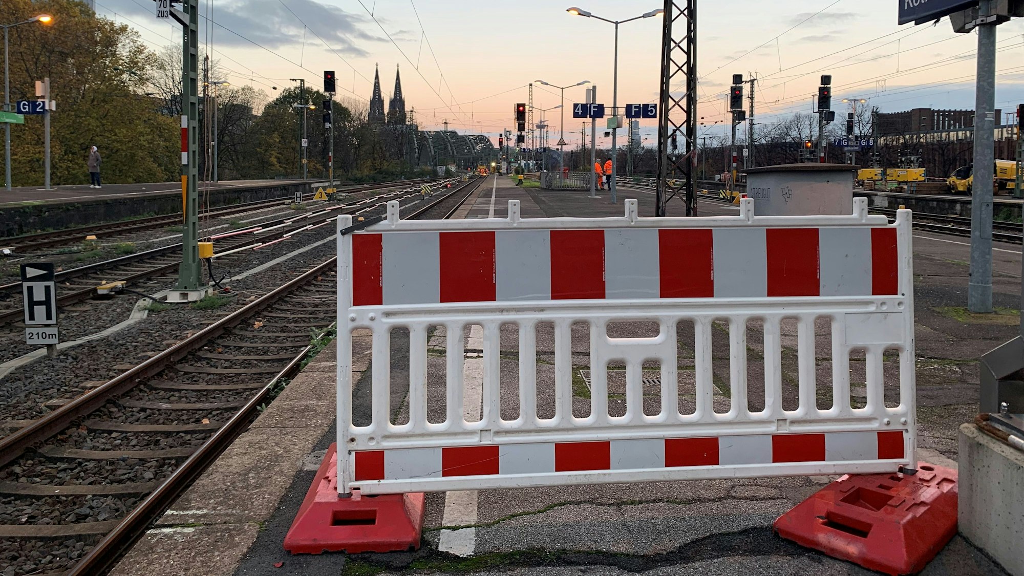 Eine Absperrung auf einem Bahnsteig des Bahnhofs Köln-Messe/Deutz ist zu sehen; dahinter in der Ferne die Spitzen des Kölner Doms.
