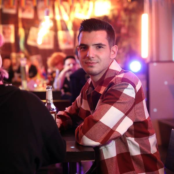 Zwei queere Jugendliche an der Bar des Kölner Jugendzentrums „Anyway“. Links mit dem Rücken zur Kamera sitzt Kitti, mit pinken Zöpfen. Daneben sitzt David im karierten Hemd und schaut in die Kamera.