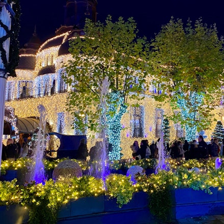 Auf einer Eisbahn umgeben von bunt beleuchteten Gebäudefassaden im Phantasialand laufen einige Menschen auf Schlittschuhen.