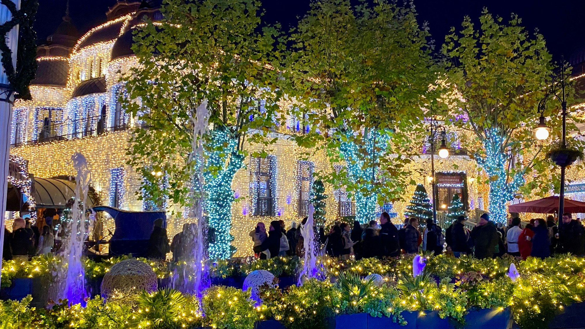 Auf einer Eisbahn umgeben von bunt beleuchteten Gebäudefassaden im Phantasialand laufen einige Menschen auf Schlittschuhen.