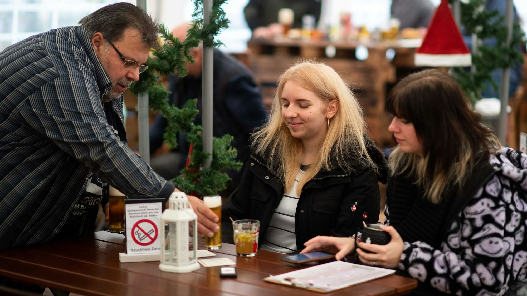 Wirt Helmut Wagner stellt einem weiblichen Gast ein Kölsch hin. Ihre Freundin trägt Winterjacke.