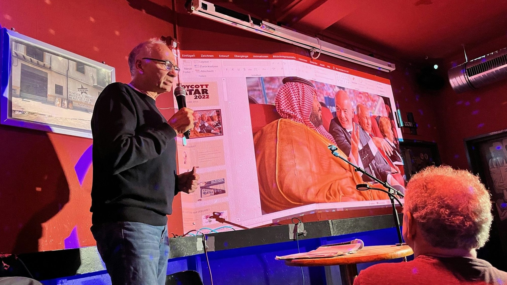 Dietrich Schulze-Marmeling hält einen Vortrag vor Publikum, im Hintergrund sieht man eine Power-Point-Präsentation