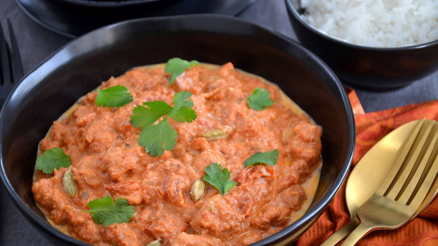Ein indisches Hähnchen-Curry steht in einer Schüssel auf dem Tisch, mit Koriander bestreut.