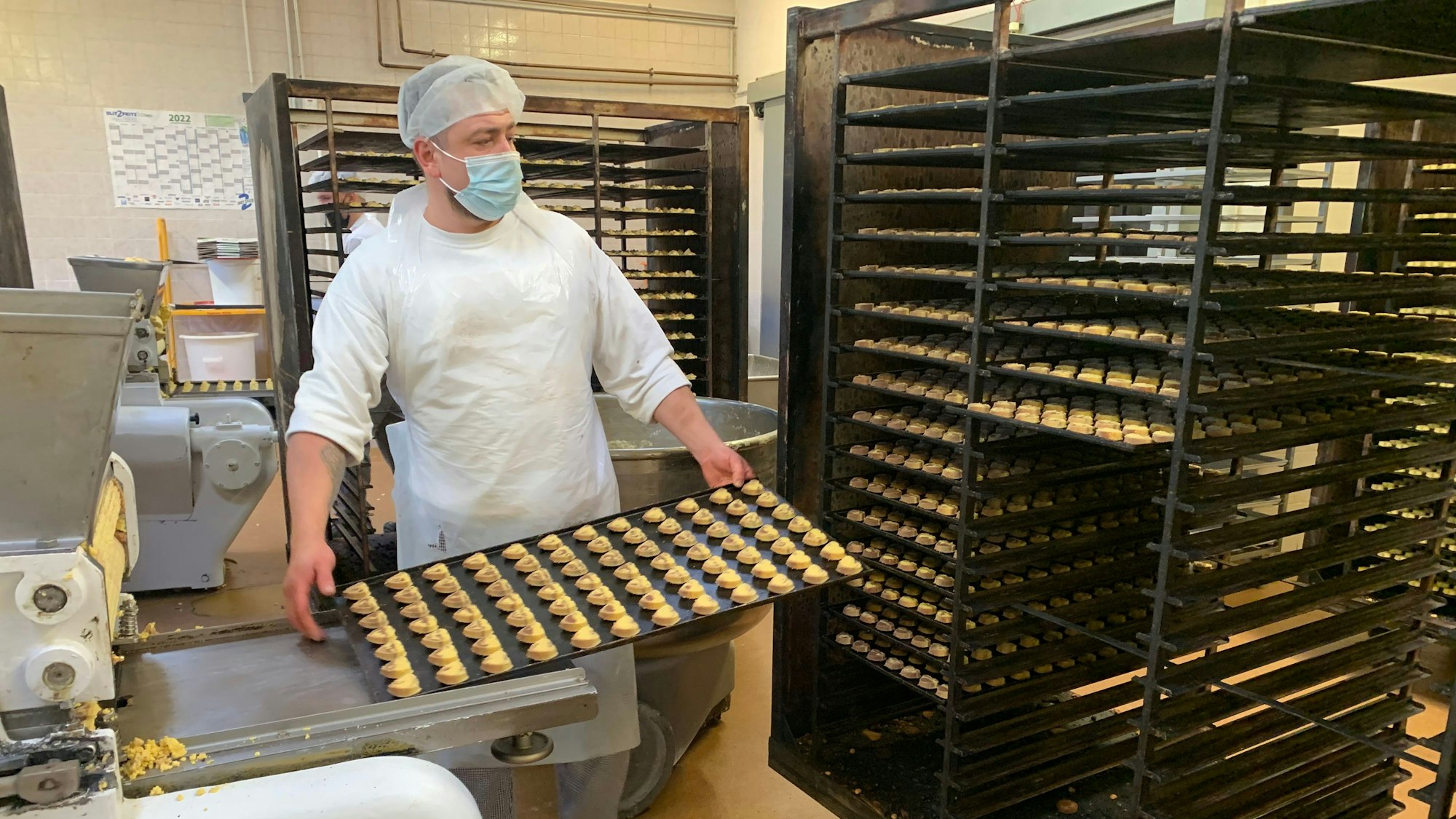 Ein Mitarbeiter der Keksfabrik hat ein Blech voll mit Keksen in der Hand.