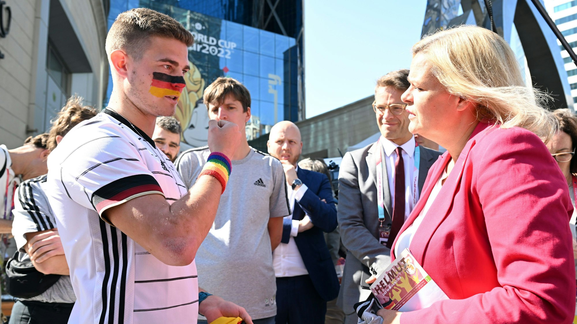 Der Kölner Student Bengt Kunkel im Gespräch mit der Bundesinnenministerin Nancy Faser. Kunkel trägt ein Schweißband mit Regenbogenfarben.