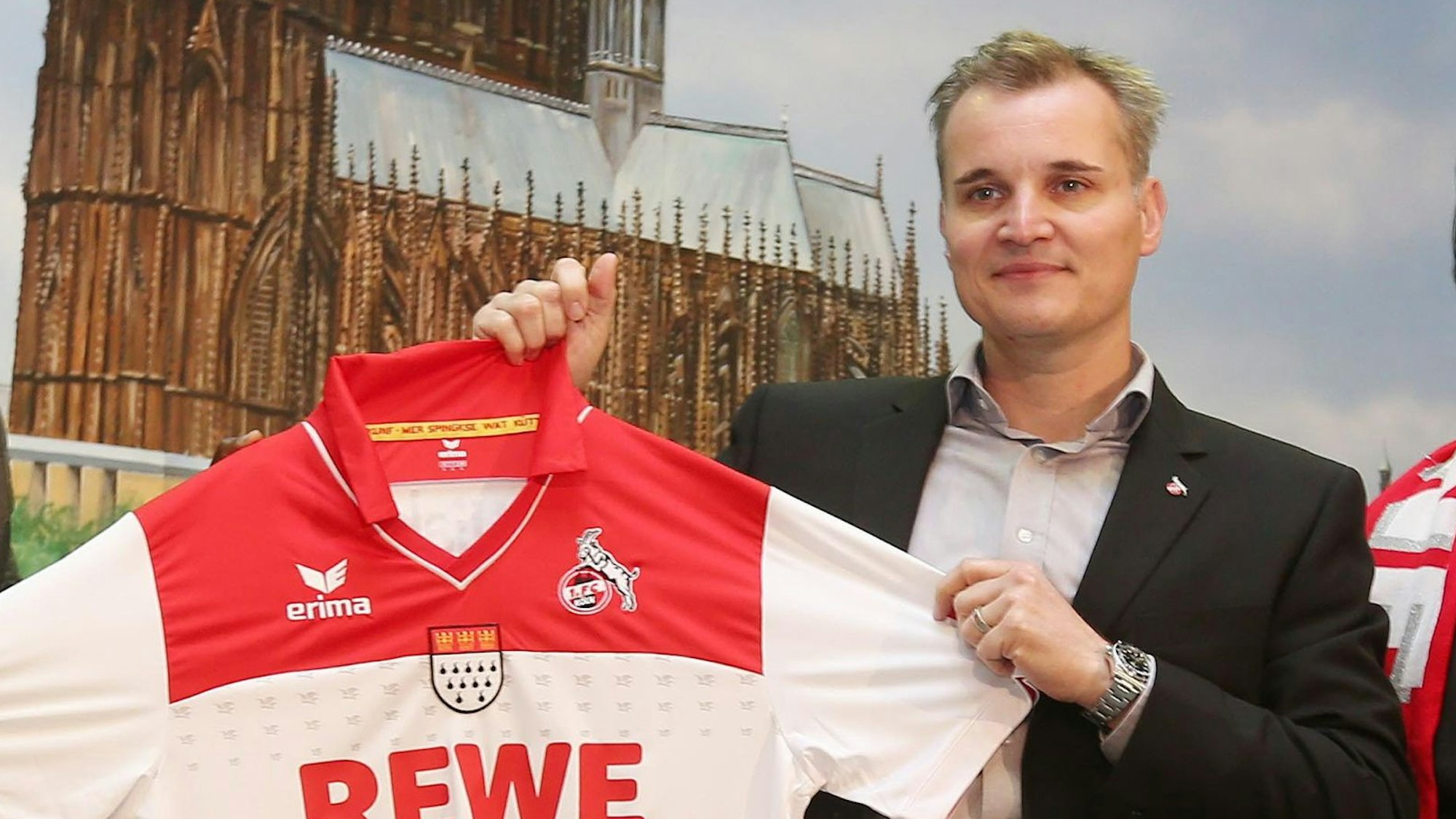 Frank Sahler, Leiter Marketing/Vertrieb beim 1. FC Köln, präsentiert ein früheres Trikot des Bundesligisten. Er hält ein rot-weißes Trikot des 1. FC Köln in der Hand.