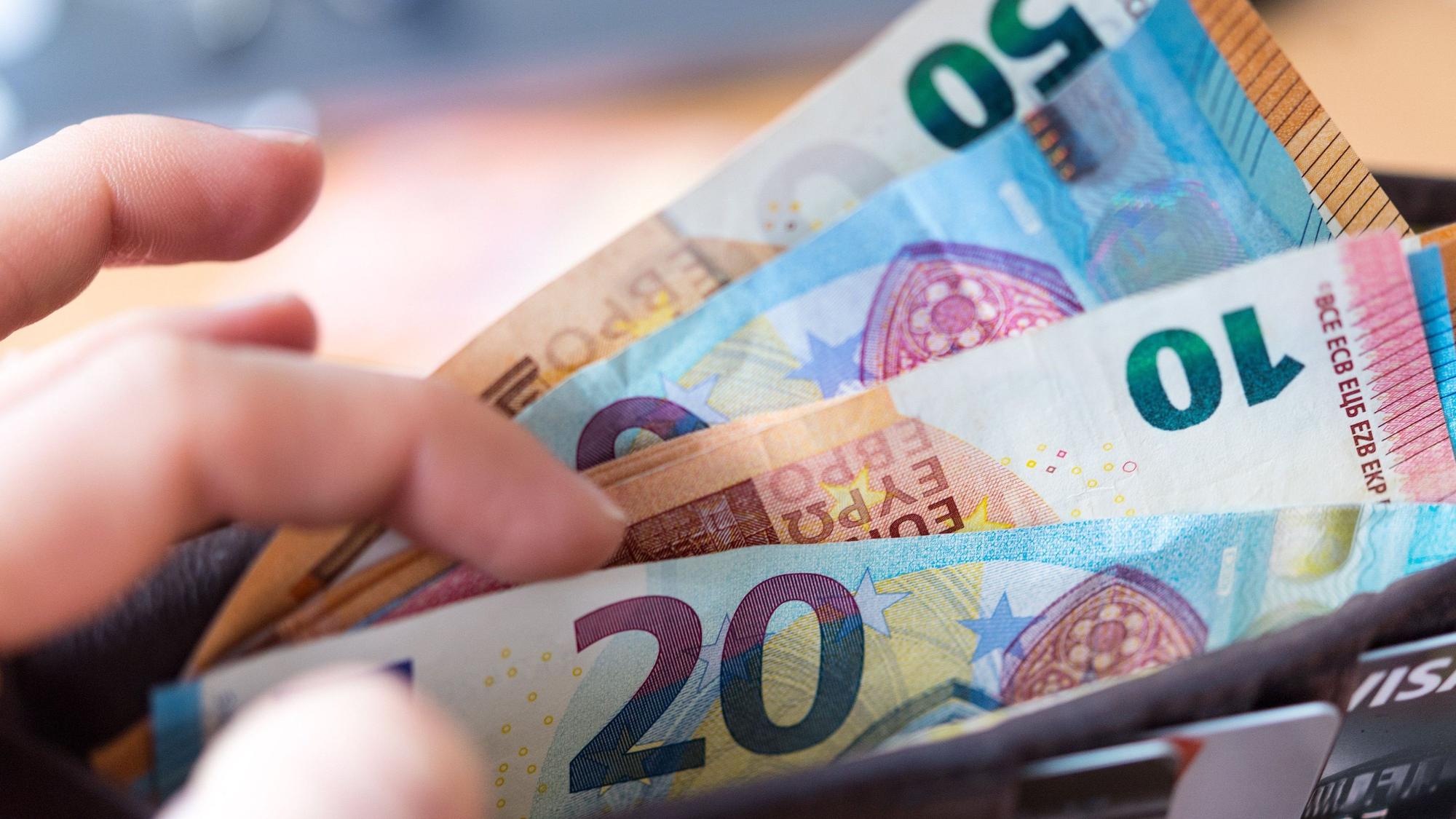 Eine Frau hält ein Portemonnaie in der Hand, in dem Geldscheine stecken.