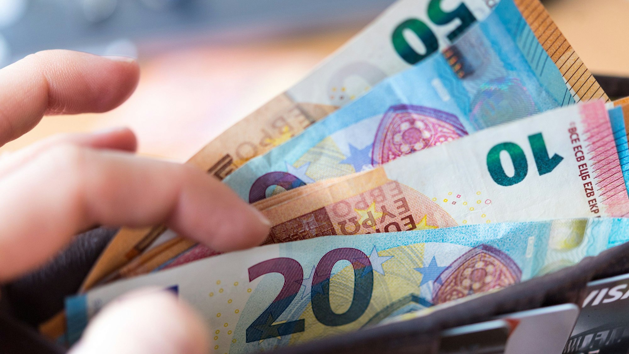 Eine Frau hält ein Portemonnaie in der Hand, in dem Geldscheine stecken.