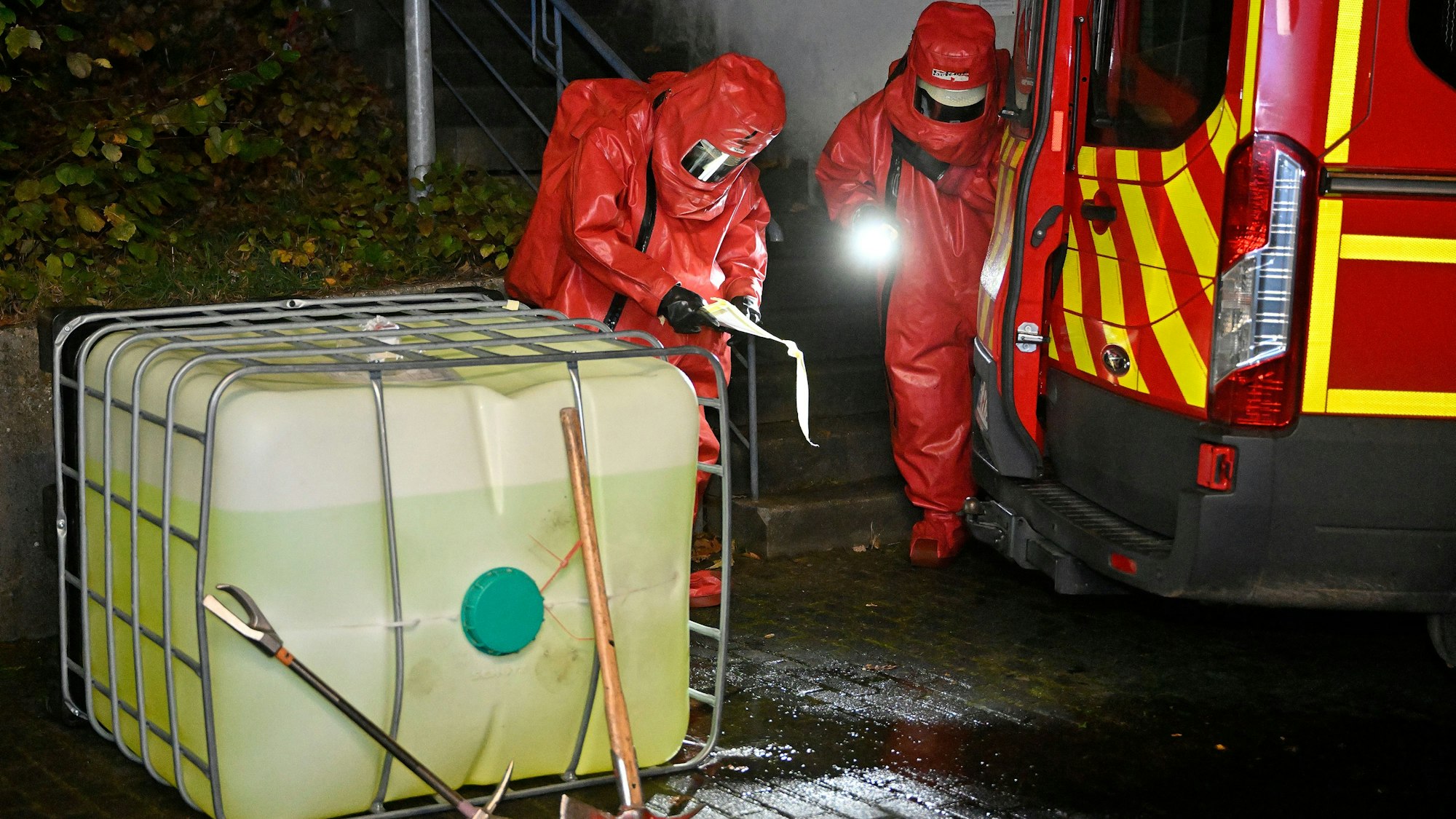Feuerwehrleute in Chemikalienschutzanzügen untersuchen einen Kunststofftank.