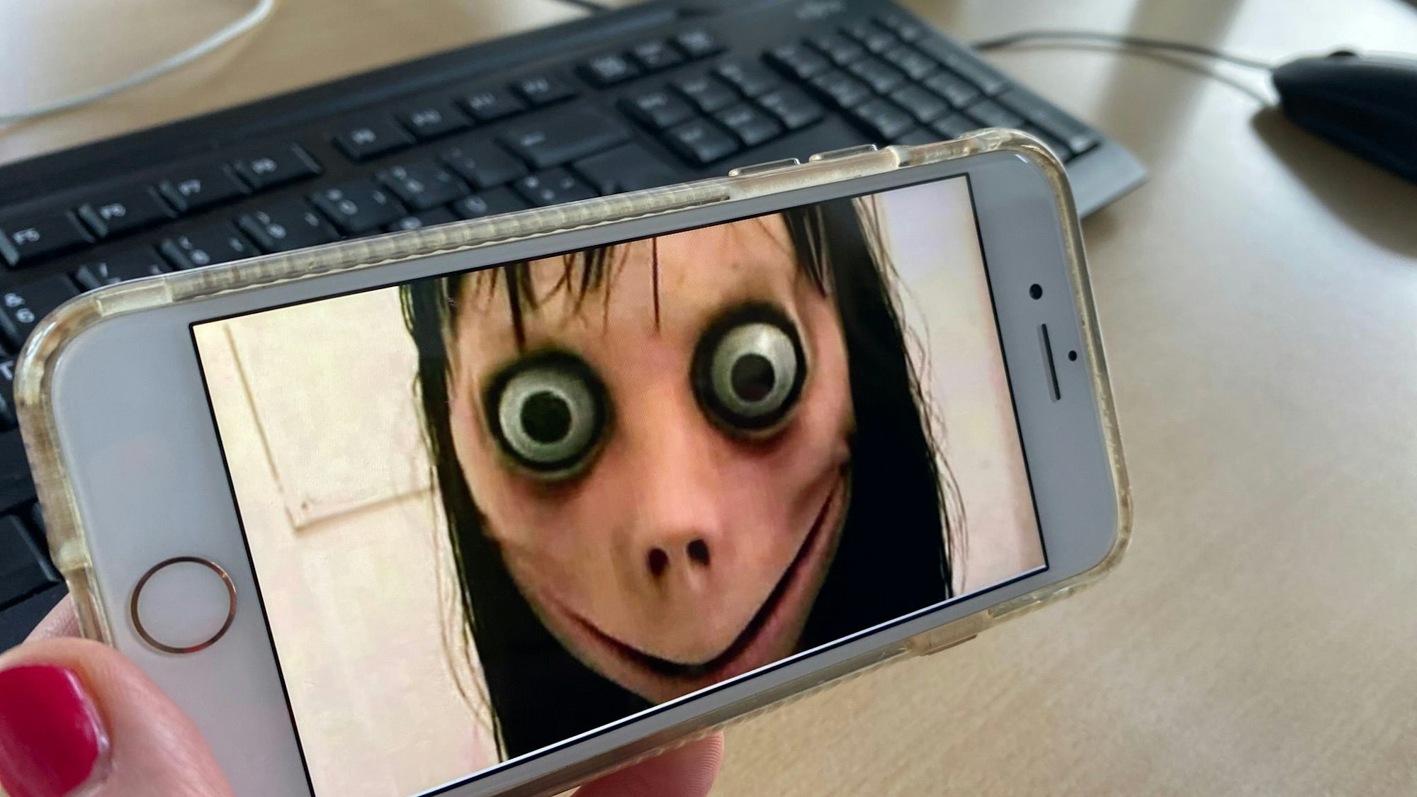 Ein Bild der Gruselfigur Momo ist auf einem Handy zu sehen.