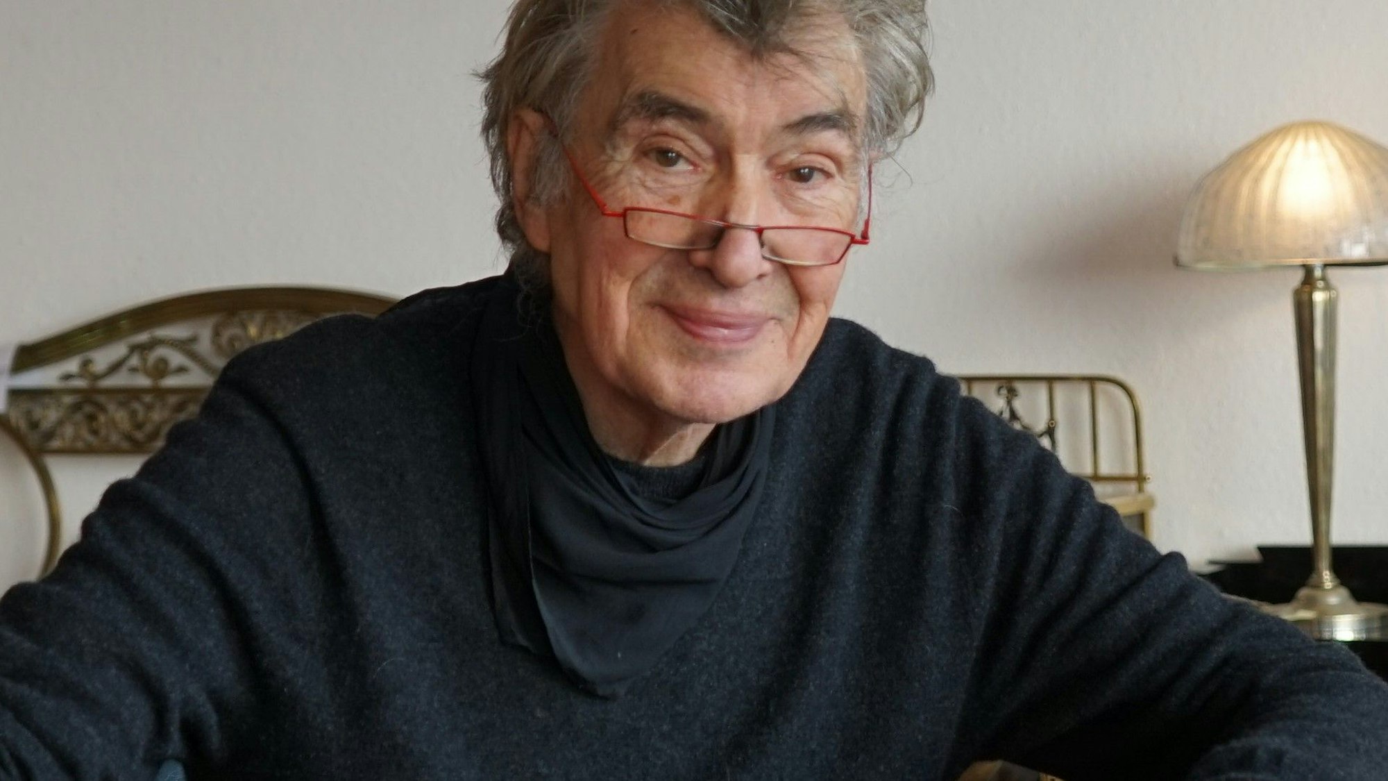 Norbert Esser sitzt an einem brauen Tisch in seinem Geschäft in Bergisch Gladbach. Hinter ihm sind allerhand Antiquitäten zu sehen.