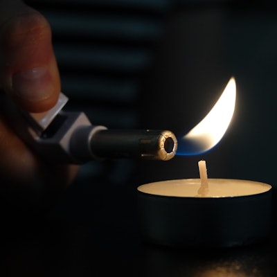 Die Flamme eines Feuerzeugs steht kurz davor einen Kerzendocht zu entzünden.