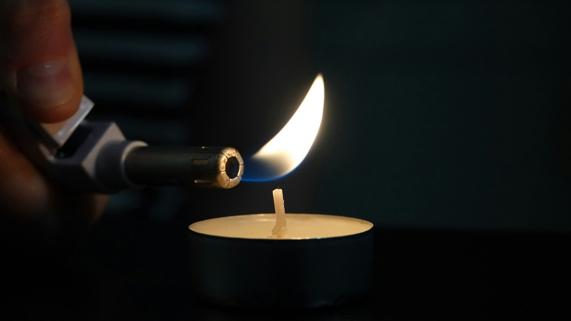 Eine Person zündet mit einem Feuerzeug ein Teelicht an.