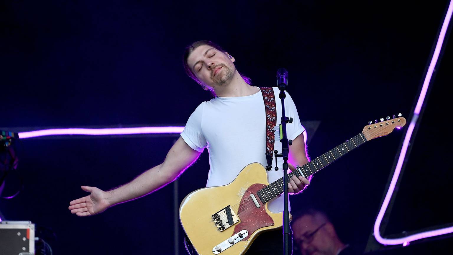 Der Sänger Philipp Poisel steht beim Auftakt der Strandkorb Open Air Tour Berlin-Brandenburg auf der Rennbahn Hoppegarten auf der Bühne. Er streckt einen Arm aus und lehnt sich mit geschlossenen Augen nach rechts. Er hat eine E-Gitarre in der linken Hand.