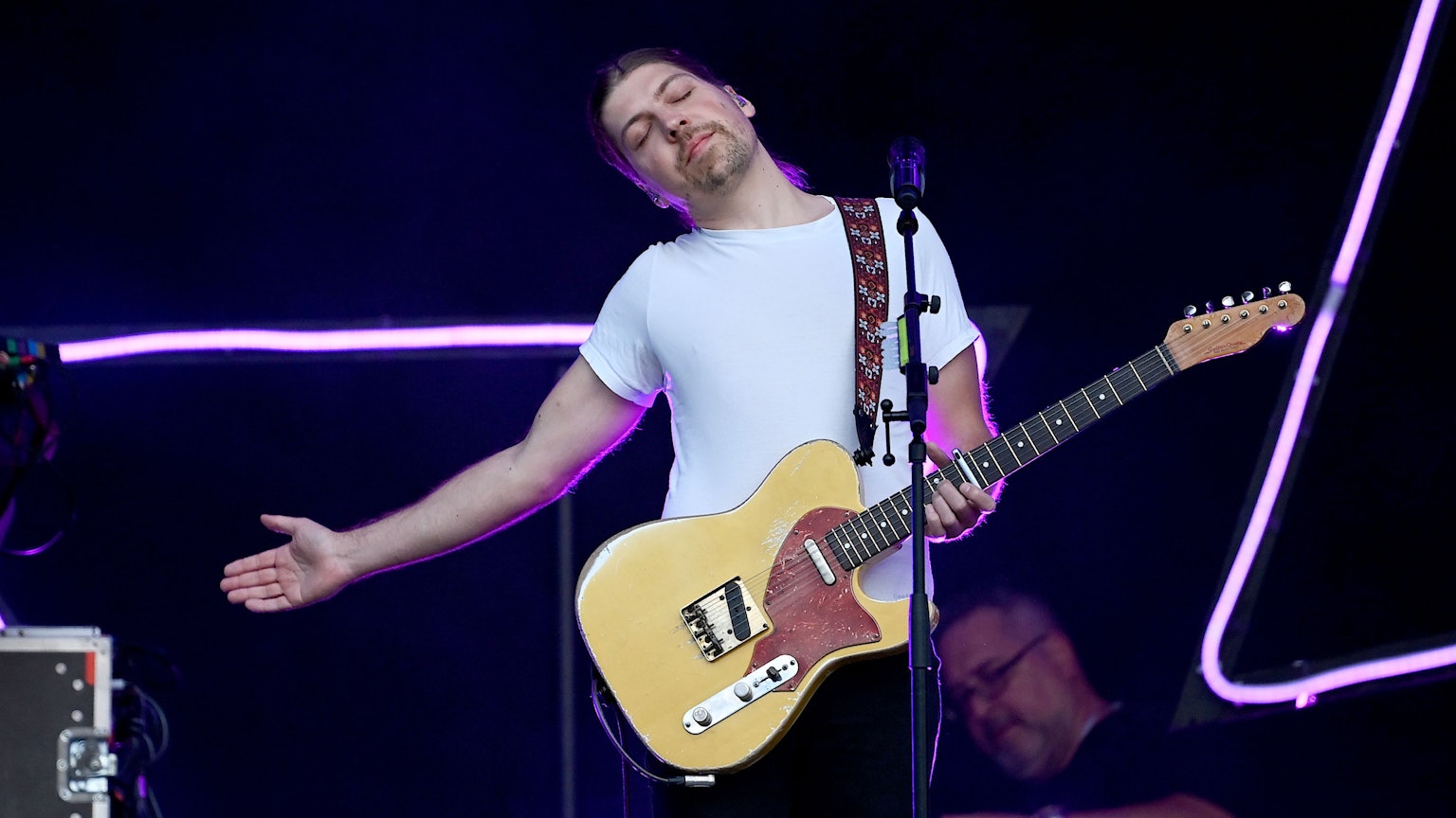 Der Sänger Philipp Poisel steht beim Auftakt der Strandkorb Open Air Tour Berlin-Brandenburg auf der Rennbahn Hoppegarten auf der Bühne. Er streckt einen Arm aus und lehnt sich mit geschlossenen Augen nach rechts. Er hat eine E-Gitarre in der linken Hand.