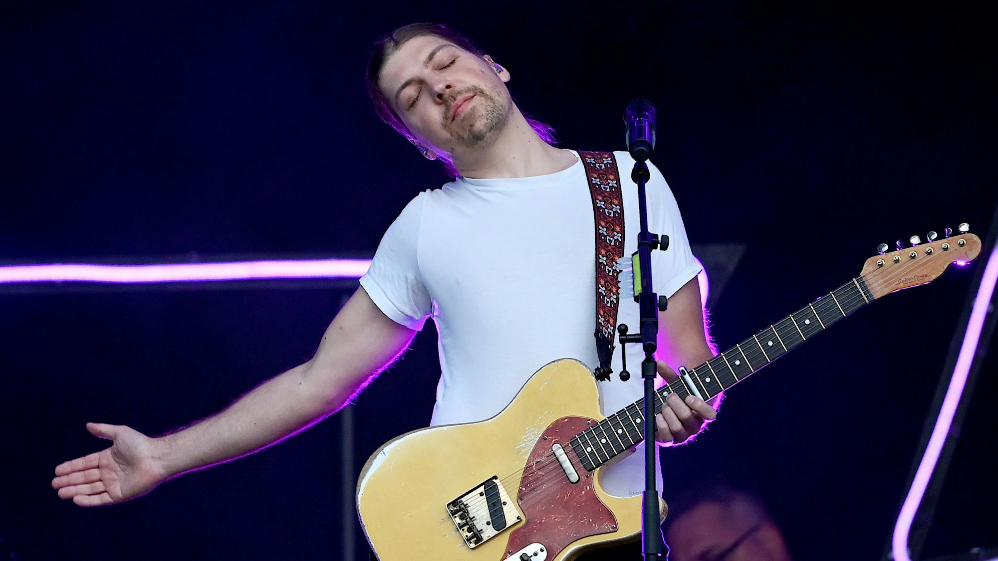 Der Sänger Philipp Poisel steht beim Auftakt der Strandkorb Open Air Tour Berlin-Brandenburg auf der Rennbahn Hoppegarten auf der Bühne. Er streckt einen Arm aus und lehnt sich mit geschlossenen Augen nach rechts. Er hat eine E-Gitarre in der linken Hand.