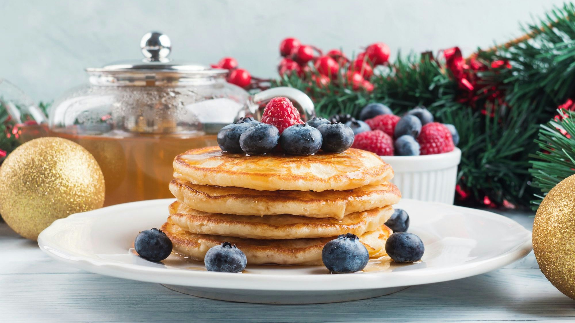 Pancakes auf einem Teller mit Blaubeeren und Tannenzweigen dekoriert.