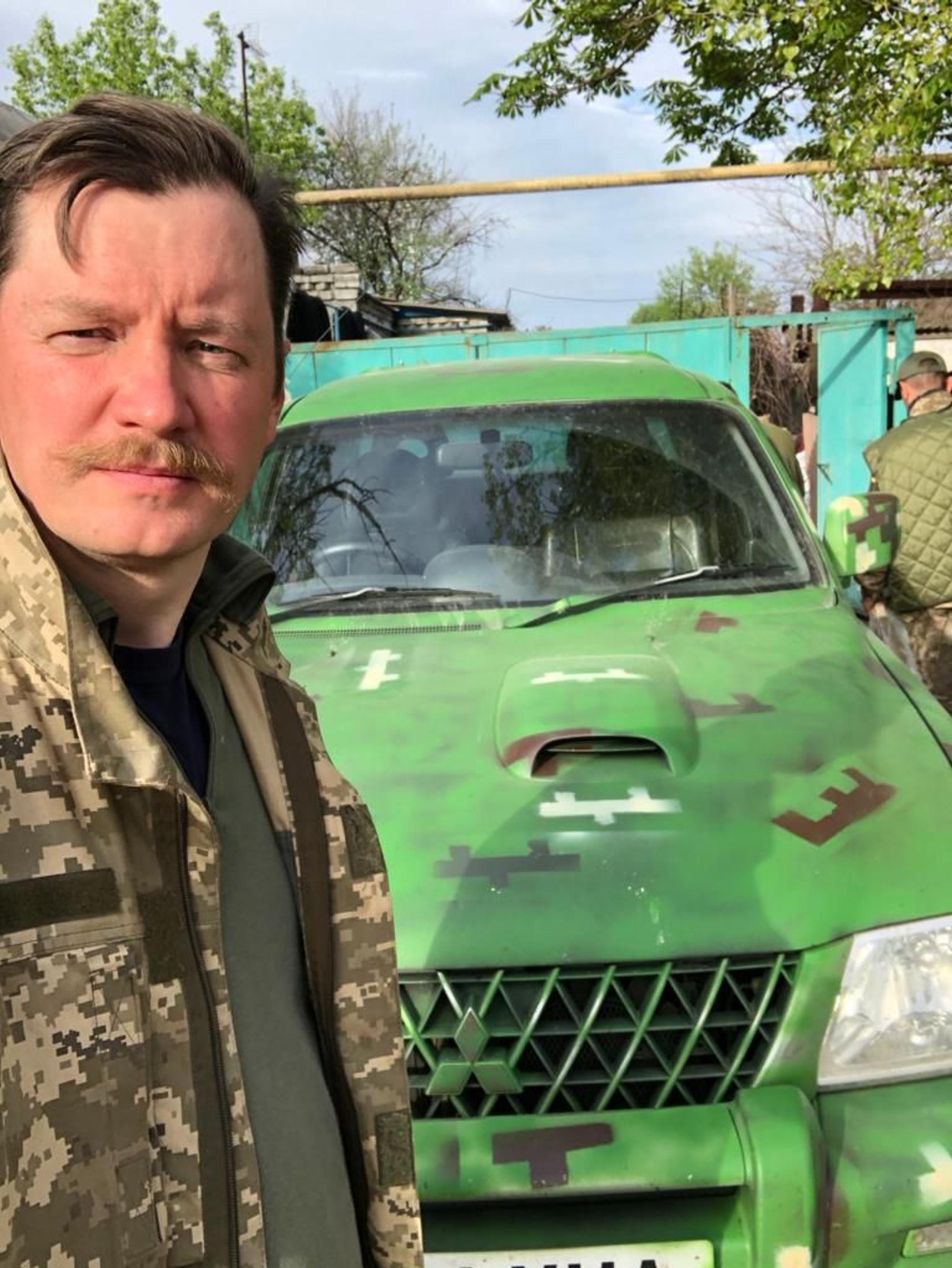 Mykola Hryhorenko steht im Flecktarn vor einem grünen Militärfahrzeug an der Front im Donbass.